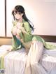 A woman in a green kimono sitting on a bed.