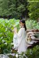 A woman in a white dress holding a fan in a garden.