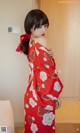 A woman in a red kimono standing in a bedroom.